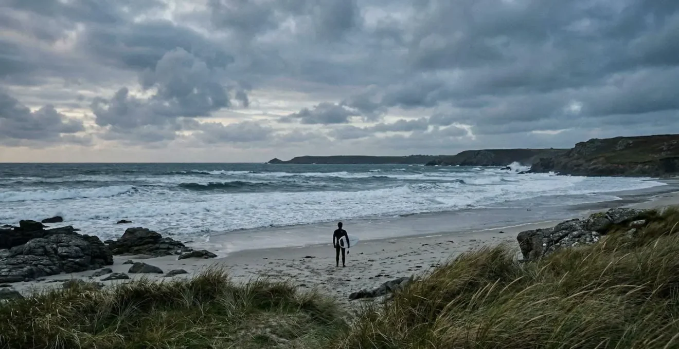 Surfeur préparant sa combinaison épaisse sur une plage bretonne sauvage avec vagues atlantiques en arrière-plan