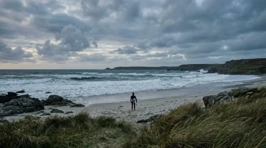 Surfeur préparant sa combinaison épaisse sur une plage bretonne sauvage avec vagues atlantiques en arrière-plan